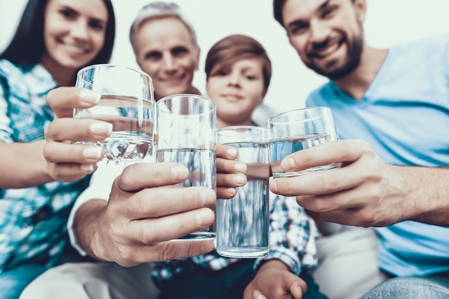 Smiling Family Drinking Water in Glasses at Home.