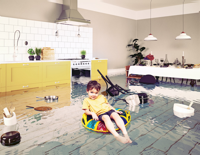 Edited photo of boy in a swim shirt and shorts sitting is a colorful inner tube in a flooded kitchen.