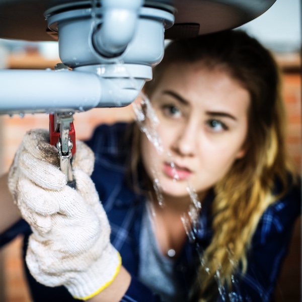 Woman fixing water leak under kitchen sink